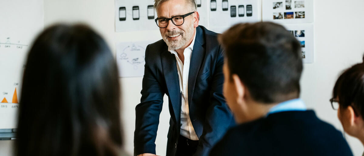 Lachender Mann im Anzug steht vor Mitarbeitern © Tom Werner / Getty Images