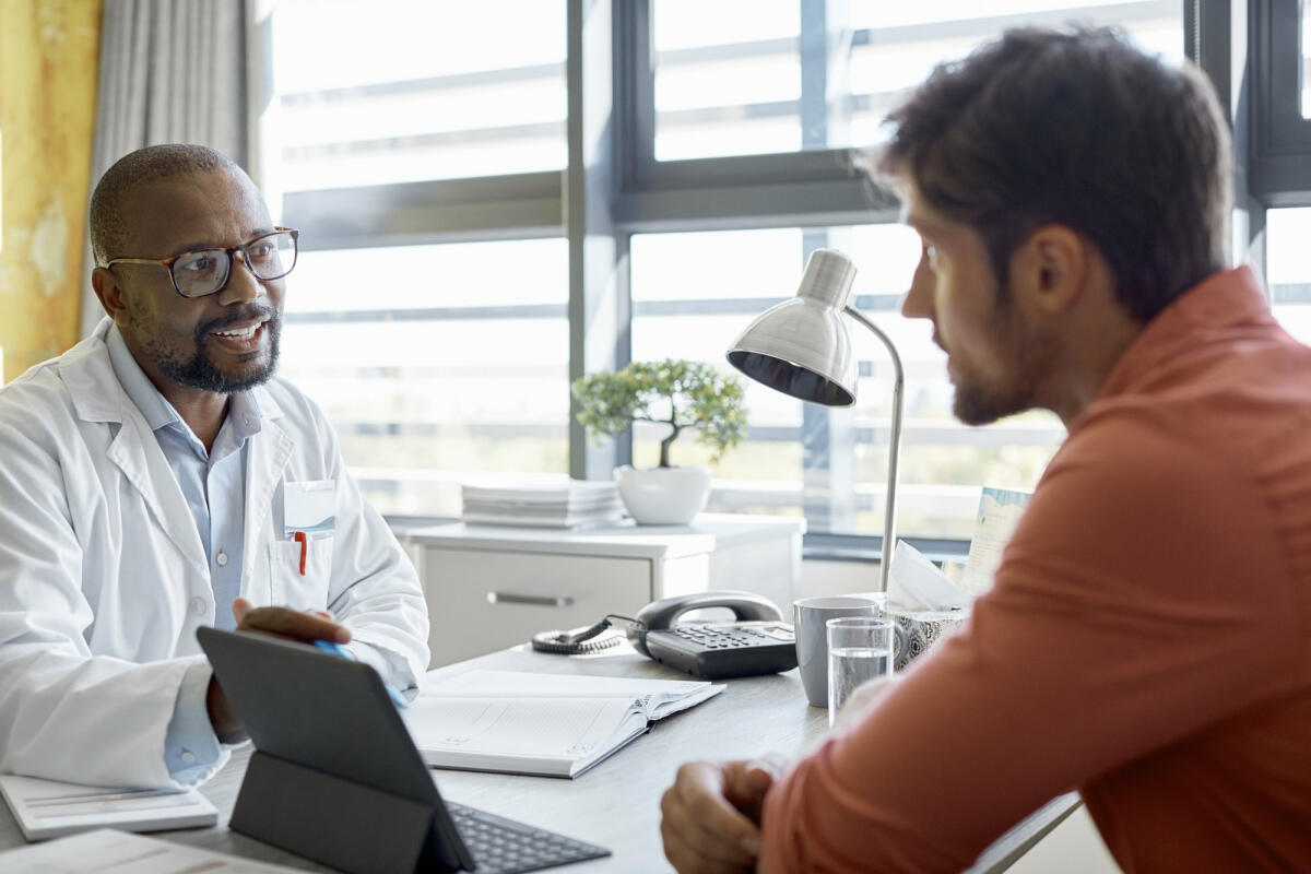 Männlicher Arzt im Gespräch mit einem Patienten in der Klinik  © Morsa Images / Getty Images