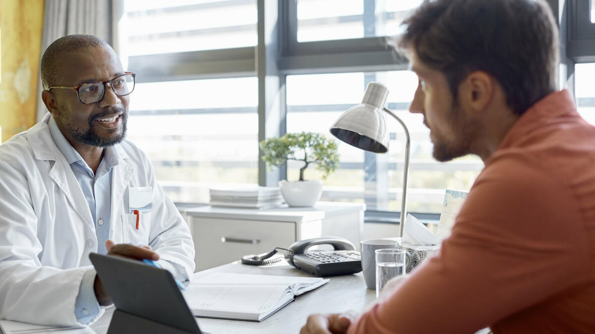 Männlicher Arzt im Gespräch mit einem Patienten in der Klinik  © Morsa Images / Getty Images