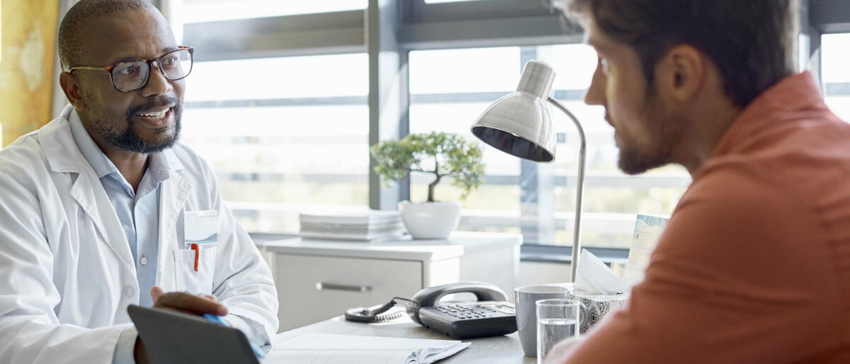 Männlicher Arzt im Gespräch mit einem Patienten in der Klinik  © Morsa Images / Getty Images