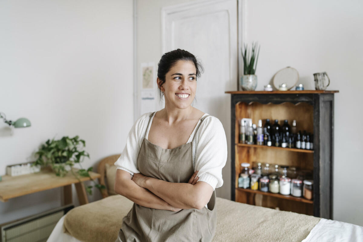 Porträt eines Bademeisters, der in einem Spa arbeitet, auf einem Massagetisch sitzt und mit verschränkten Armen wegschaut. Konzept eines Spas. © COROIMAGE/ Getty Images