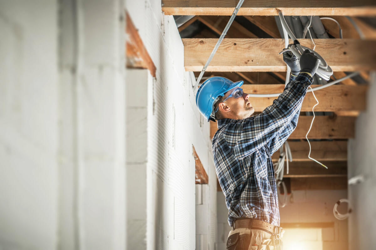 Professioneller kaukasischer Elektriker, der an der Installation der elektrischen Leitungen in der Decke eines neuen Wohnhauses arbeitet. © welcomia/ Getty Images