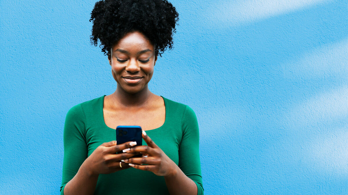 Frau benutzt Smartphone neben blauer Wand © Tim Robberts / Getty Images