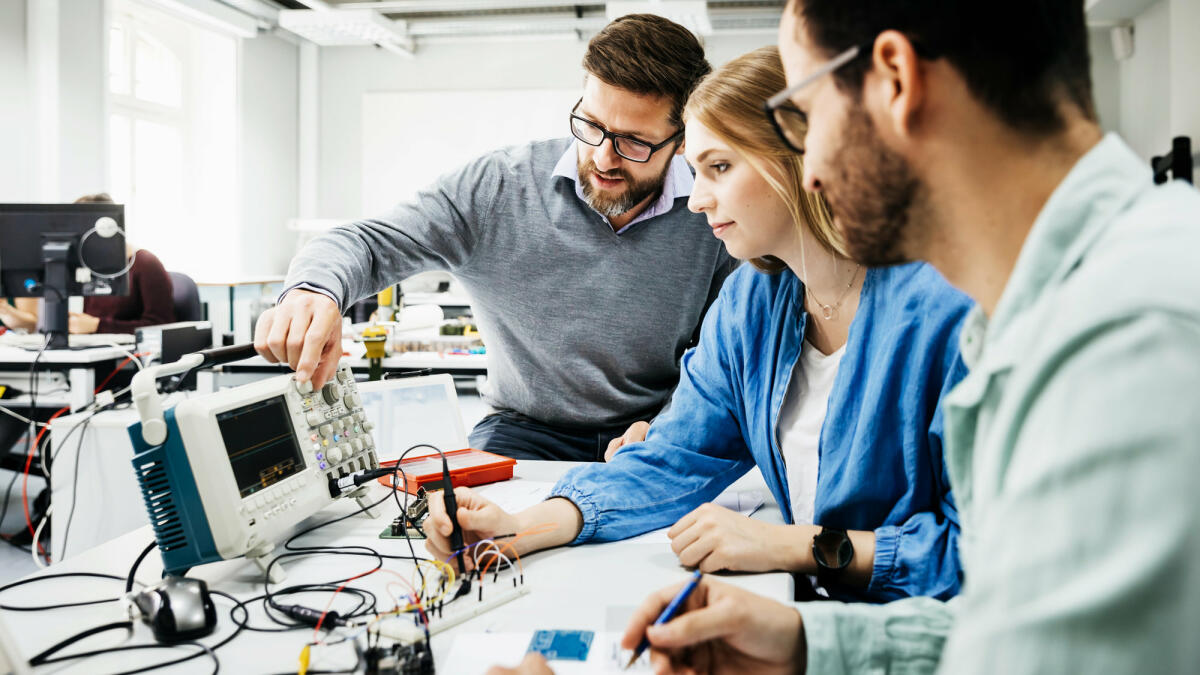 Zwei Männer und junge Frau sitzen vor technischen Geräten © Tom Werner / Getty Images