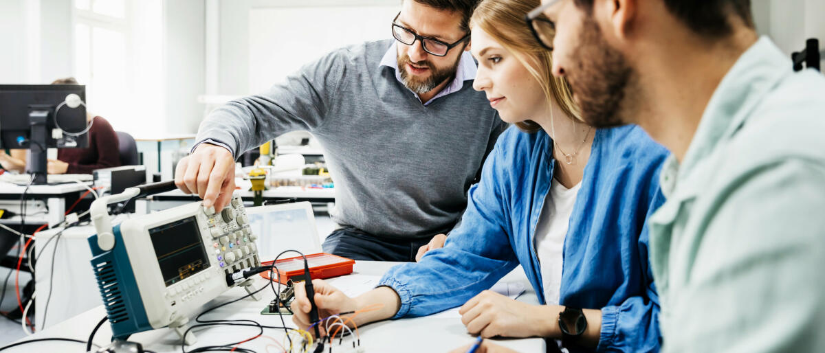 Zwei Männer und junge Frau sitzen vor technischen Geräten © Tom Werner / Getty Images