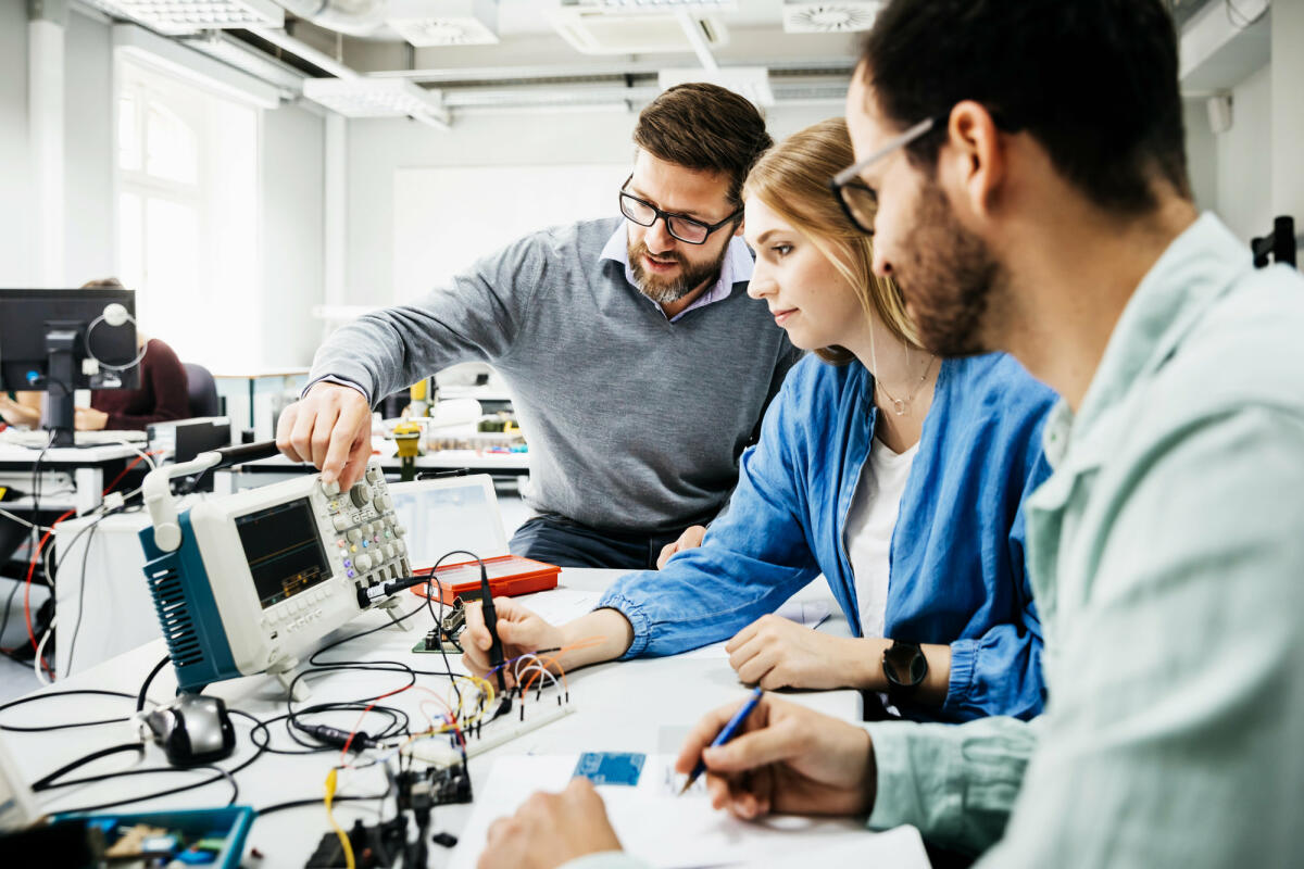 Zwei Männer und junge Frau sitzen vor technischen Geräten © Tom Werner / Getty Images