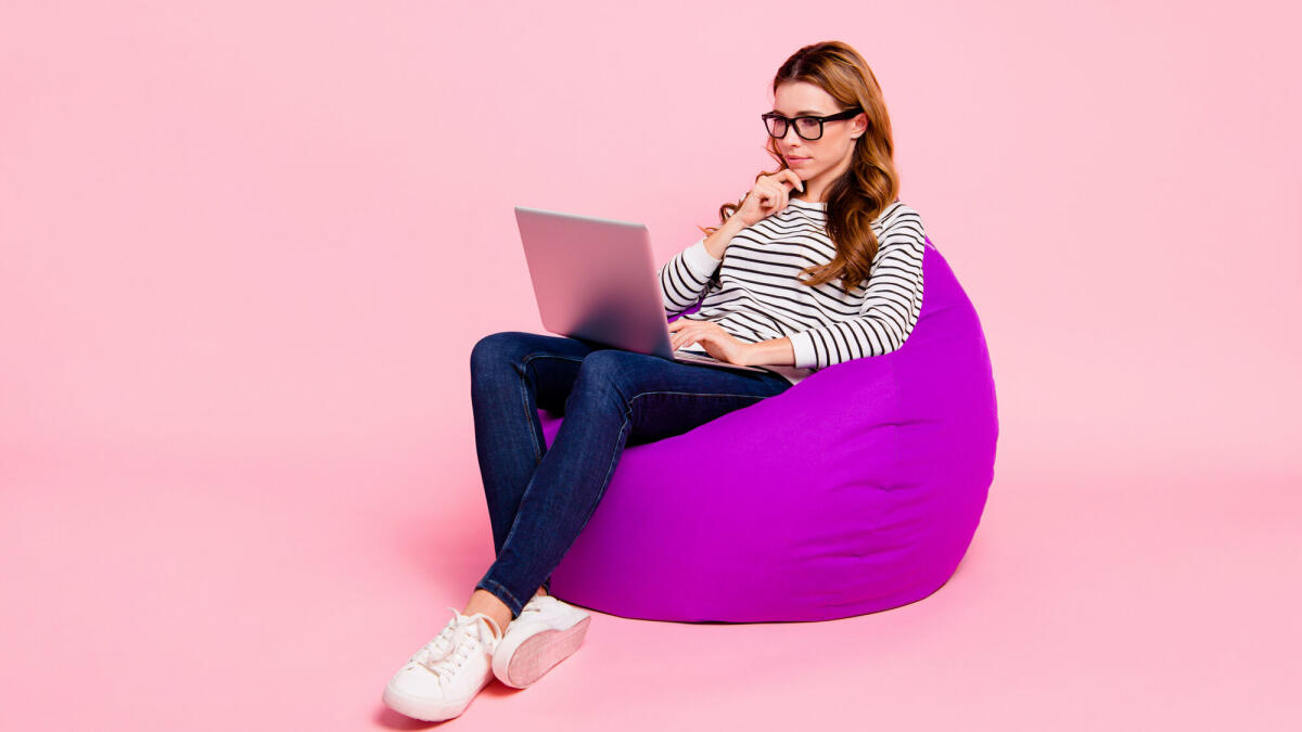 Junge Erwachsene sitzt mit ihrem Laptop auf einem Sitzsack und guckt nachdenklich © Deagreez / Getty Images