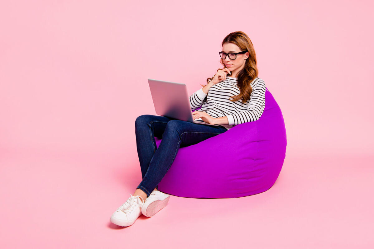 Junge Erwachsene sitzt mit ihrem Laptop auf einem Sitzsack und guckt nachdenklich © Deagreez / Getty Images