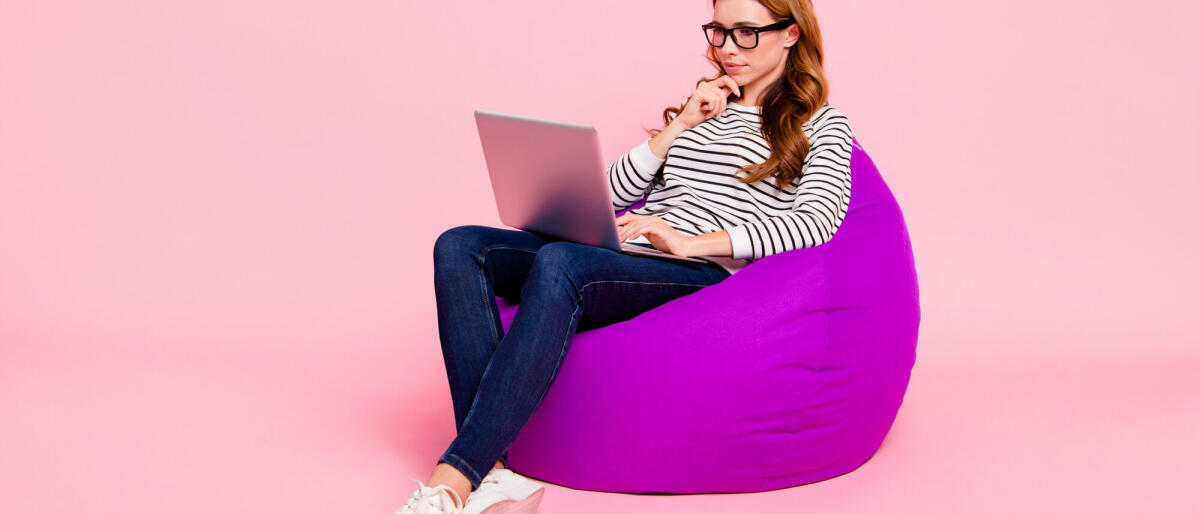 Junge Erwachsene sitzt mit ihrem Laptop auf einem Sitzsack und guckt nachdenklich © Deagreez / Getty Images