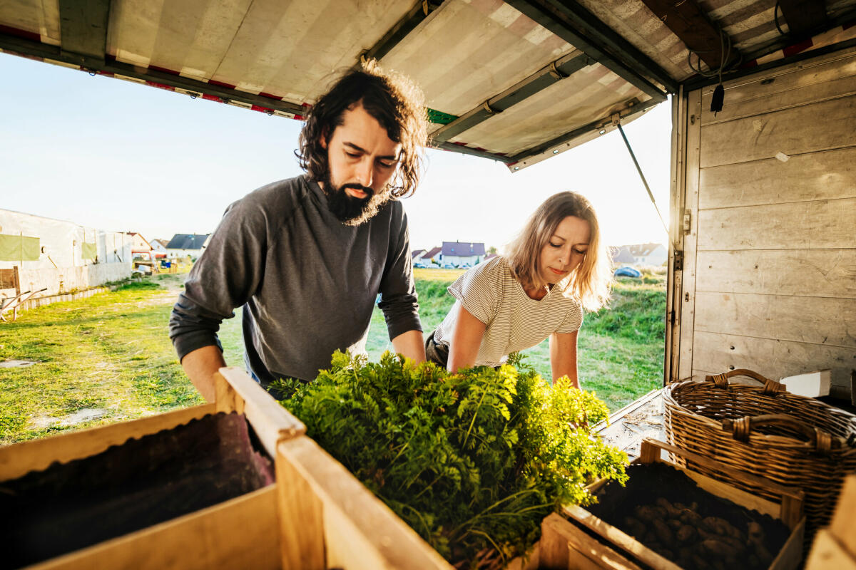 Ein paar städtische Landwirte laden Kisten mit verschiedenen frisch geernteten Waren auf einen Lastwagen und machen sich bereit, sie zum Markt zu bringen. © Getty Images/ 	Tom Werner