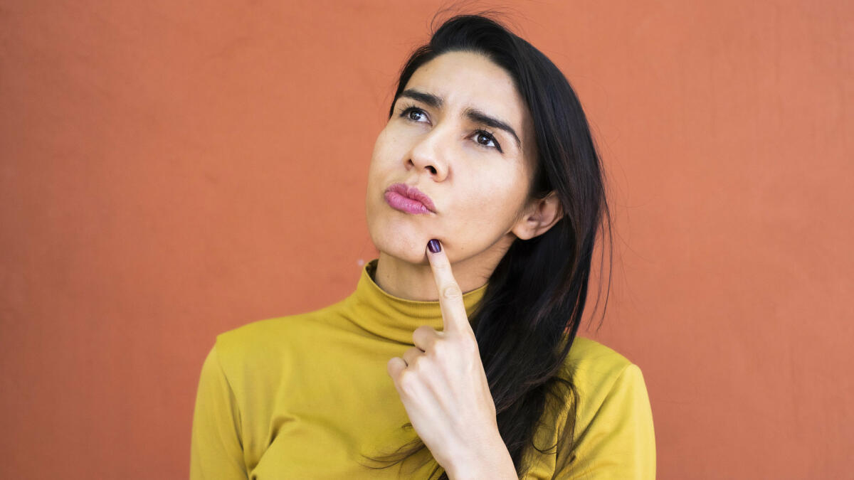 Latino-Frau in Gedanken versunken, nachdenklich und aufblickend, Finger am Kinn © Sergio Mendoza Hochmann / Getty Images