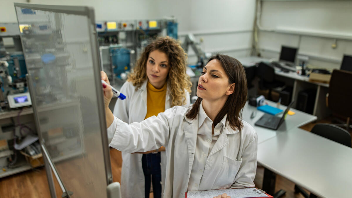 Ingenieure am arbeiten und eine schreibt auf Whiteboard im mechanischen Labor  © chabybucko/ Getty Images